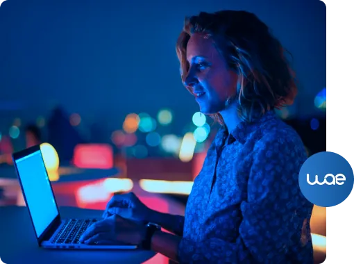 Mulher usando notebook à noite, com o logo da WAE