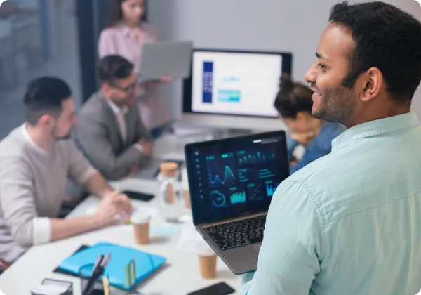 Profissional com notebook exibindo painéis de dados em reunião de equipe