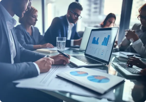 Equipe em reunião analisando gráficos no notebook e em relatórios